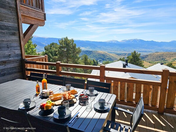 A wooden deck with a table set for breakfast, overlooking a mountainous landscape.