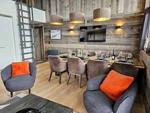 A dining area with a wooden wall, a TV mounted above a table set for six, and a ladder in the corner.