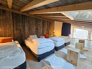 A rustic bedroom with wooden beams, a large bed, two smaller beds, and a view of the outdoors.