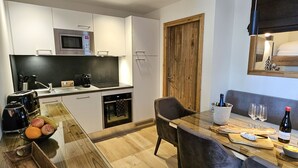 A modern kitchen with a microwave, oven, and a dining area with a table set for two. - Appartement T2-Cabine B-02 - Collection Cassiopée (Font-Romeu-Odeillo-Via)