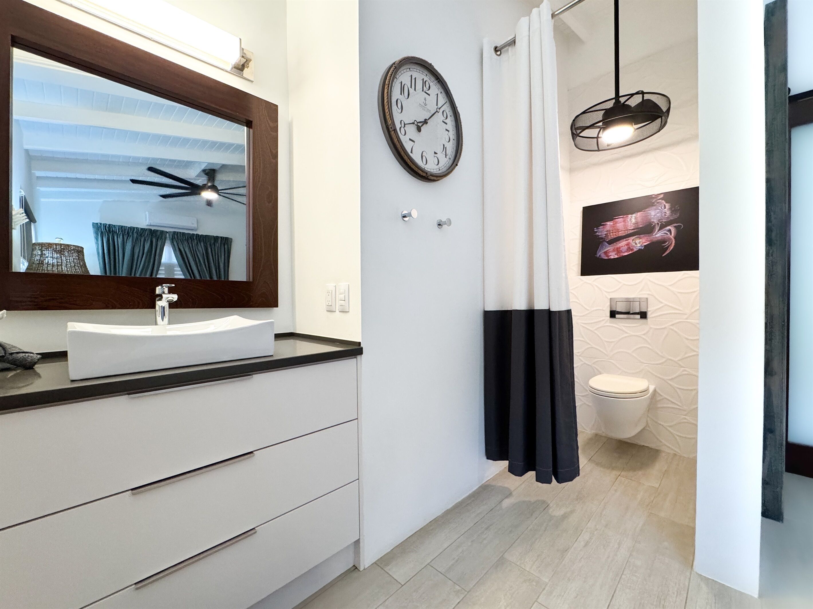 A modern bathroom with a large mirror, a clock, a sink, and a toilet.