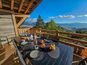 Un espace extérieur aménagé pour prendre les repas, avec une table pour deux, entouré d’une terrasse en bois offrant une vue panoramique sur les montagnes.