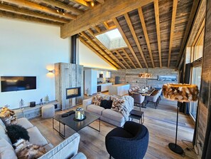 A modern living space with a high ceiling, a fireplace, a dining area, and a kitchen.