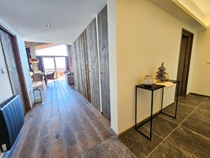 Un couloir doté d’un plancher en bois, une table en métal noir agrémentée d’objets décoratifs et une vue sur un coin repas.