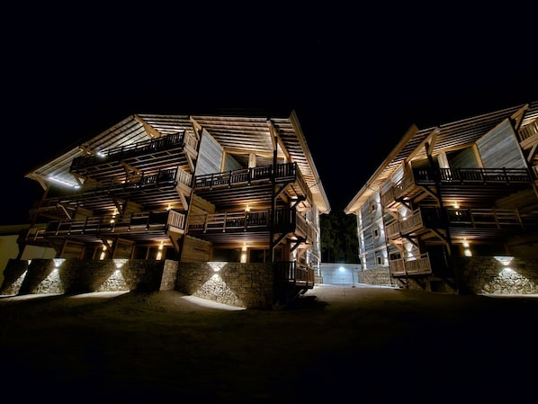 Vue nocturne d’un chalet traditionnel en bois, doté de plusieurs balcons et de fondations en pierre.