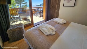 A hotel room with a bed, a small stool, a table with chairs, and a view of the outdoors. - Appartement B-13 T2 Cabine (Font-Romeu-Odeillo-Via)