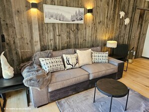 A cozy living room with a wooden wall, a sofa with patterned cushions, a side table, and a small round table.