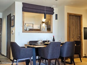 A dining area with a table set for four, a large mirror above the table, and a wooden door to the right.