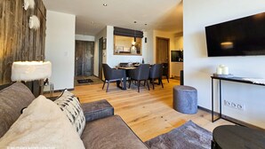 A modern living room with a sofa, a dining table with chairs, a TV mounted on the wall, and a wooden floor. - Appartement B-13 T2 Cabine (Font-Romeu-Odeillo-Via)