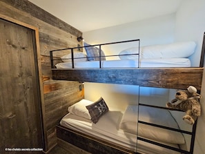 Quarto com beliches de madeira, um urso de pelúcia no beliche inferior e um espelho no beliche superior.