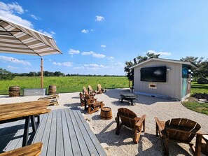 Eine Außenpatio-Terrasse mit Holzmöbeln, einem Feuerkorb und einem Fernsehbildschirm.