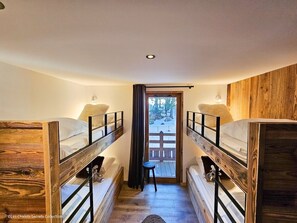 A dormitory room with bunk beds, a small stool, and a door leading to an outdoor area.