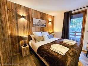 A bedroom with a wooden wall panel, a bed with a brown blanket, white pillows, and a framed picture above the bed. - Appartement A-11 T4 (Font-Romeu-Odeillo-Via)