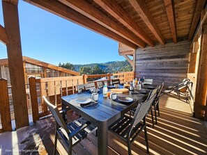 Terraza de madera con una mesa lista para comer, con vistas a un paisaje montañoso.