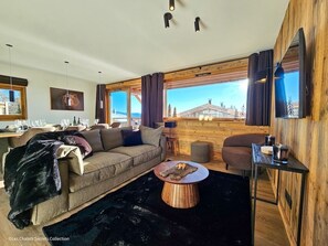 A cozy living room with a sofa, a round wooden coffee table, and a TV mounted on a wooden wall.