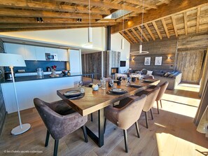 Una cocina moderna con una isla central, suelo de madera y una zona de comedor con una mesa larga y sillas.