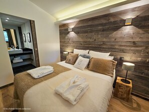 Un dormitorio moderno con cabecera de madera, cama bien hecha con toallas y una mesita de noche con lámpara.
