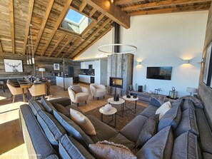 Amplia sala de estar con techo alto, chimenea y cocina moderna al fondo.