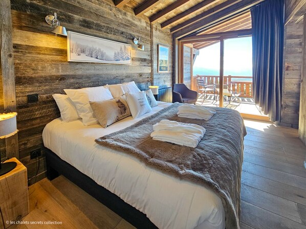 A wooden cabin bedroom with a large bed, a wooden headboard, and a view of the outdoors.