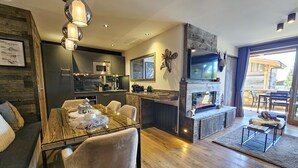 Una cocina moderna con armarios oscuros, una isla central y un comedor con una mesa de vidrio y sillas acolchadas.