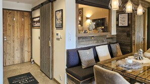 Una sala moderna con una mesa de comedor de vidrio, un sofá con cojines, una puerta de madera y un espejo que refleja la habitación.