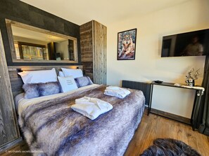 A bedroom with a large bed, a mirror, a TV, and a deer head decoration. - Appartement T2-CABINE A-02 - Collection Cassiopée (Font-Romeu-Odeillo-Via)