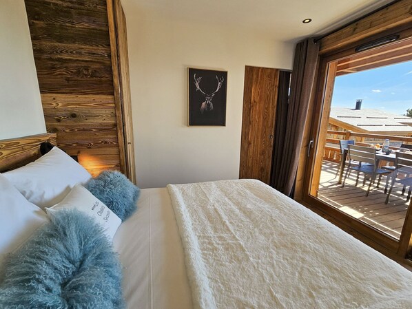 A bedroom with a large bed, a wooden headboard, a framed picture on the wall, and a view of an outdoor deck.