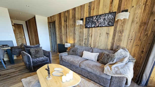 A modern living room with a wooden wall panel, a grey sofa, a wooden coffee table, and a fireplace.