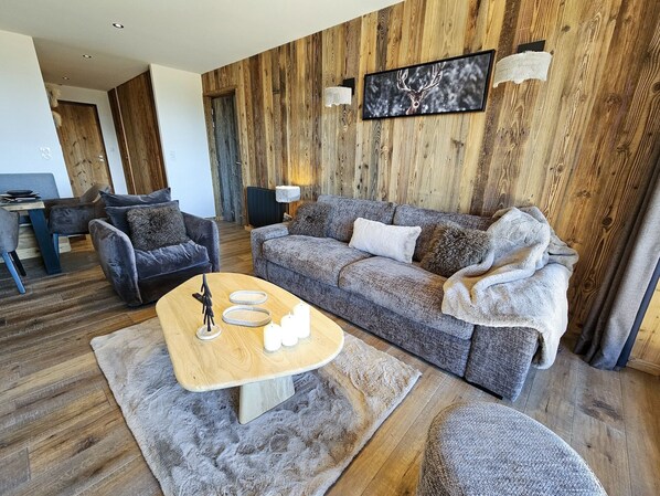 A modern living room with a wooden wall panel, a grey sofa, a wooden coffee table, and a fireplace.