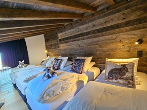 A large, cozy bedroom with wooden walls and a rustic ceiling. There are three beds with white linens and decorative pillows, including one with a rabbit design.