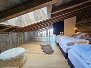 Um quarto com pé-direito alto, vigas de madeira, um claraboia e uma cama com um ursinho de pelúcia.