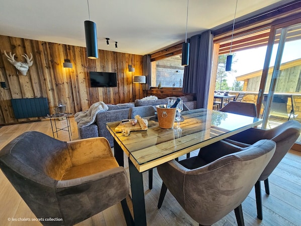 A modern living room with a wooden wall, a glass dining table, and comfortable seating.