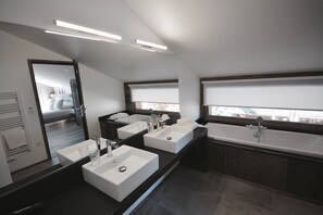 Un baño moderno con dos lavamanos, una bañera y un espejo grande.