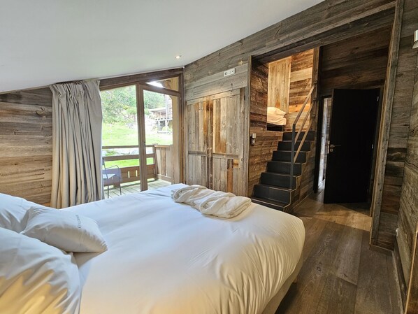 Un dormitorio con una cama grande, paredes de madera, una escalera que conduce a un altillo y vistas al exterior.