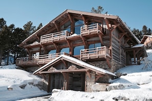 Una cabaña de madera de varios niveles con balcones, cimientos de piedra y un paisaje cubierto de nieve.