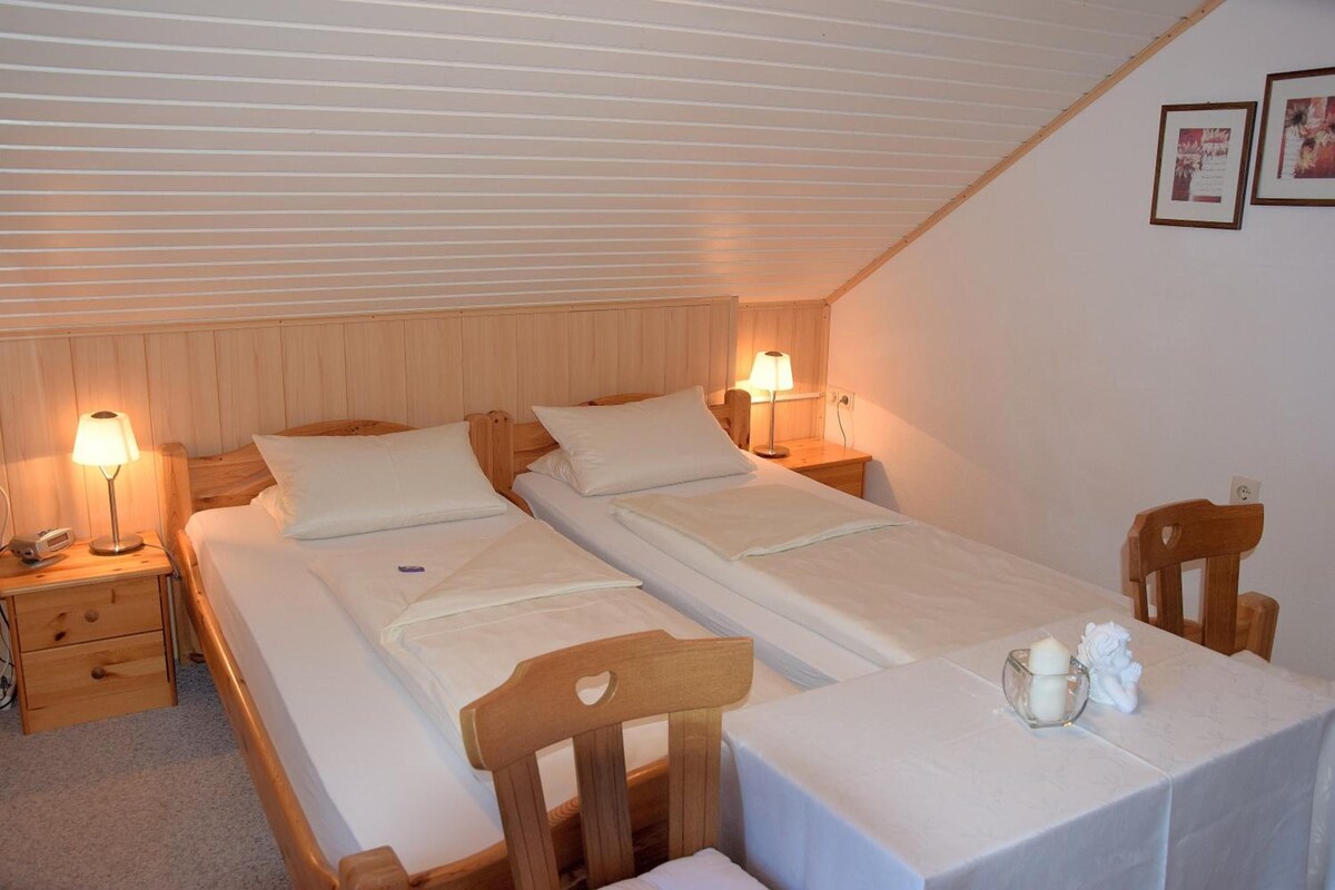Une chambre avec deux lits, des têtes de lit en bois, des lampes de chevet, une petite table avec une bougie et une chaise.