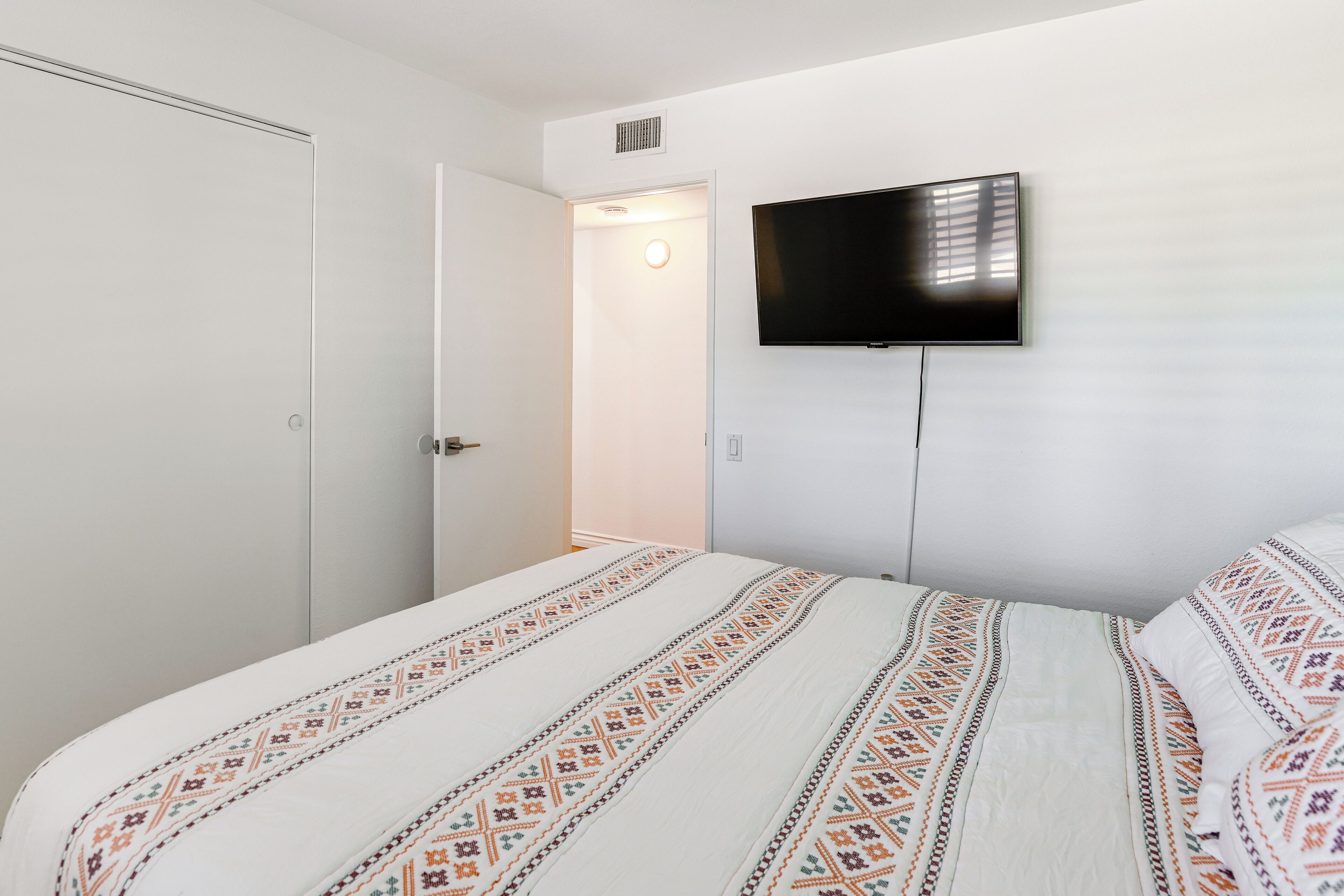 A bedroom with a bed, a television mounted on the wall, and a door leading to another room.