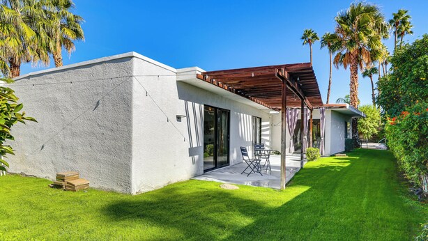A modern house with a white exterior, a covered patio, and a well-maintained lawn.