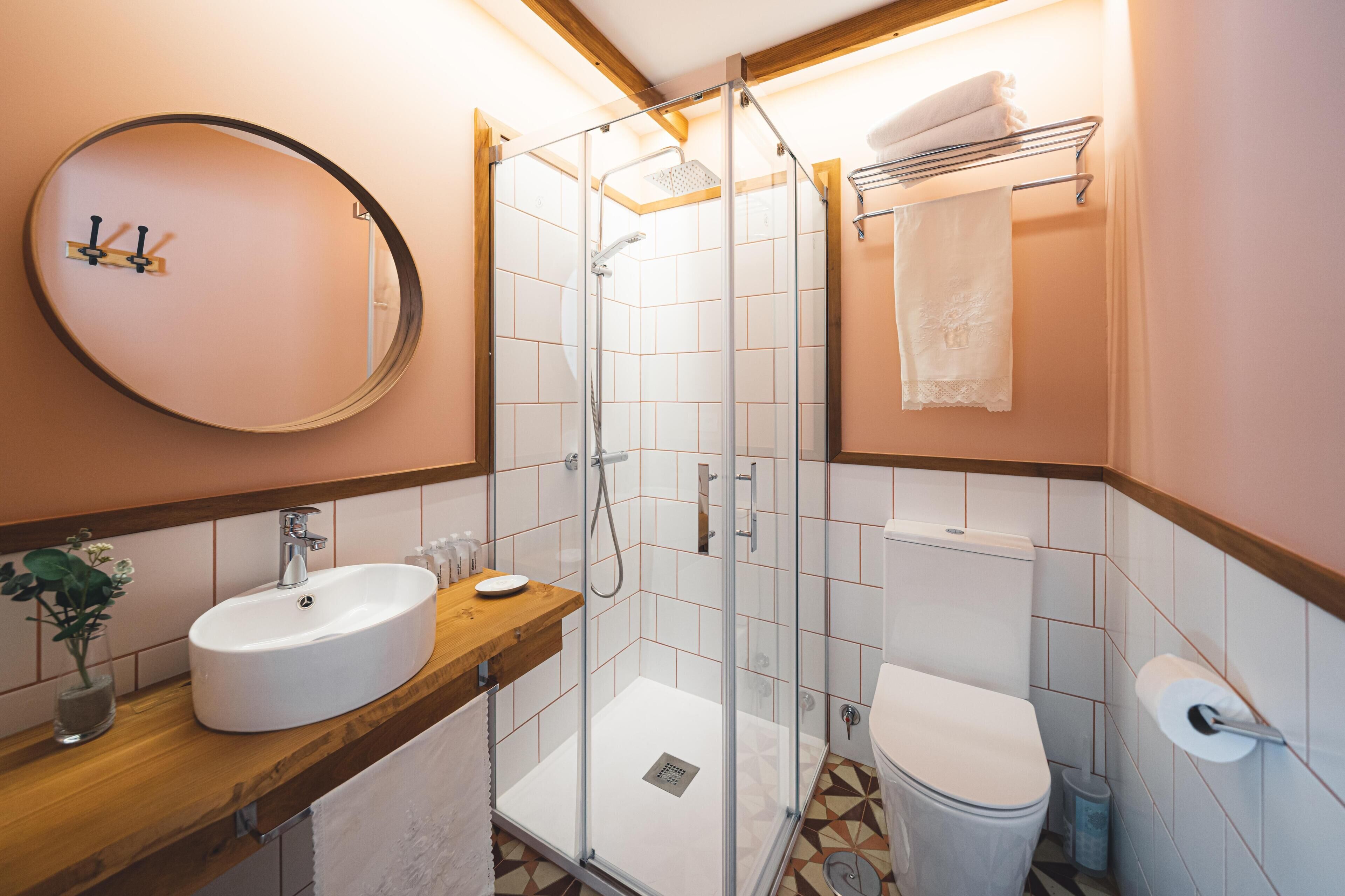 A bathroom with a glass-enclosed shower, a sink with a wooden countertop, a toilet, and a mirror on the wall.