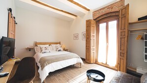 A bedroom with a bed, wooden floor, a desk with a chair, a small table, and a wardrobe with a mirror.