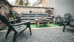 An outdoor seating area with a grey sofa, two black chairs, a wooden table, and a small potted plant. - Maison de Campagne 4 Avec Terrain de Pétanque, Idéal Pour les Familles et Amis (Vireux-Wallerand)