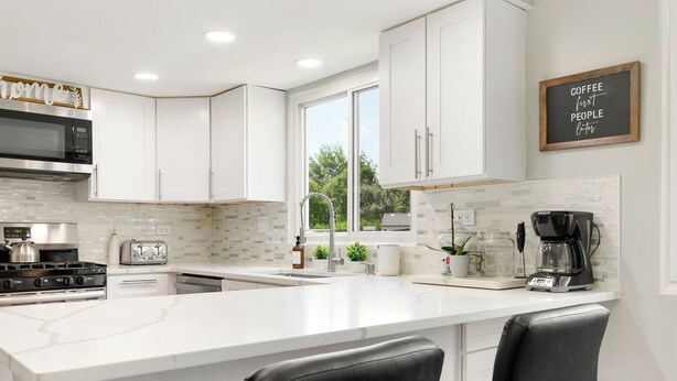 A modern kitchen with white cabinetry, a large island with bar stools, a coffee machine, and a view of the outdoors.