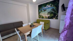 A small, modern room with a wooden dining table, white chairs, a green sofa, and a large tropical mural on the wall.