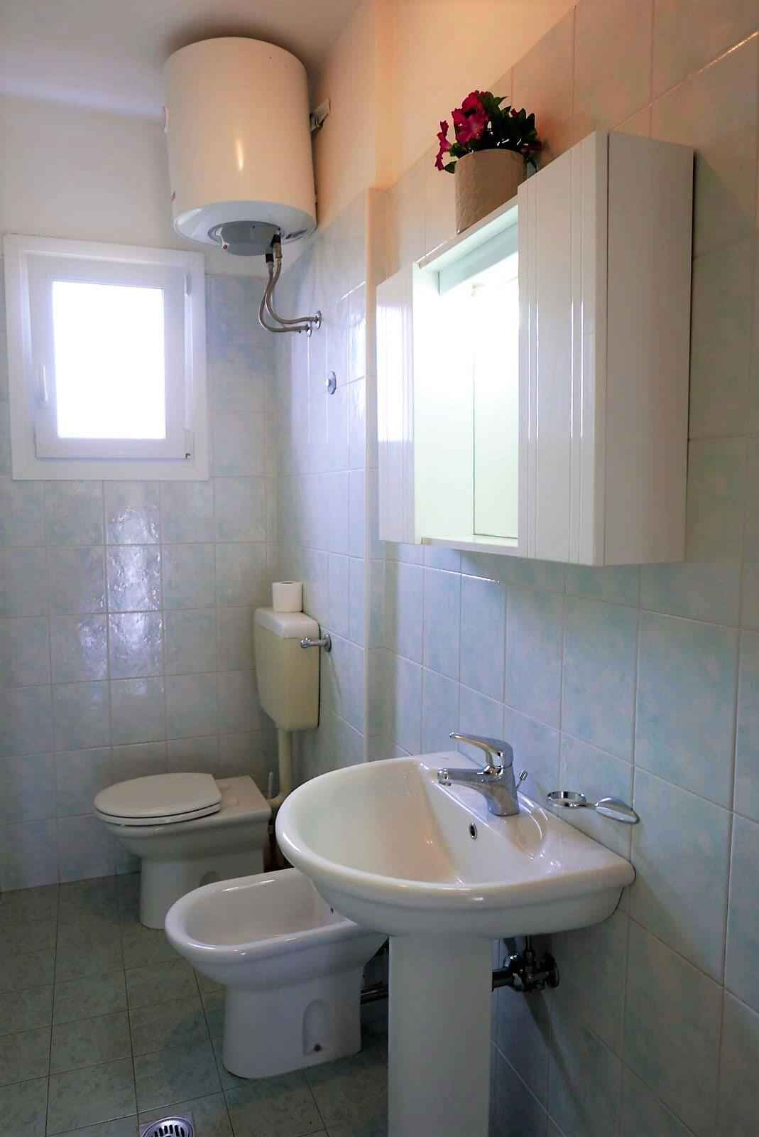 Een badkamer met toilet, bidet, wastafel en een raam.