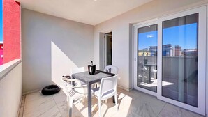 Un balcón con mesa y sillas, una puerta corrediza de vidrio y vistas a edificios.