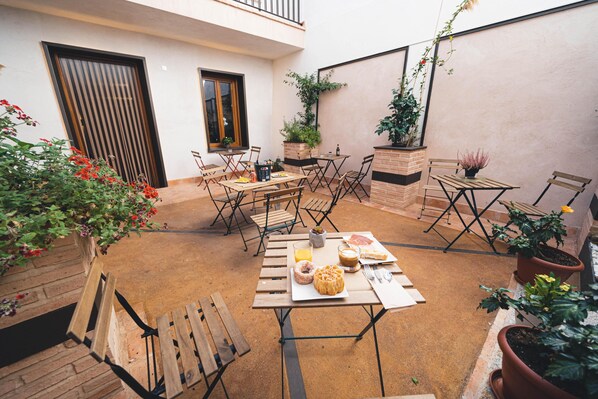 Un patio al aire libre con mesas y sillas de madera, plantas en macetas y una variedad de alimentos.