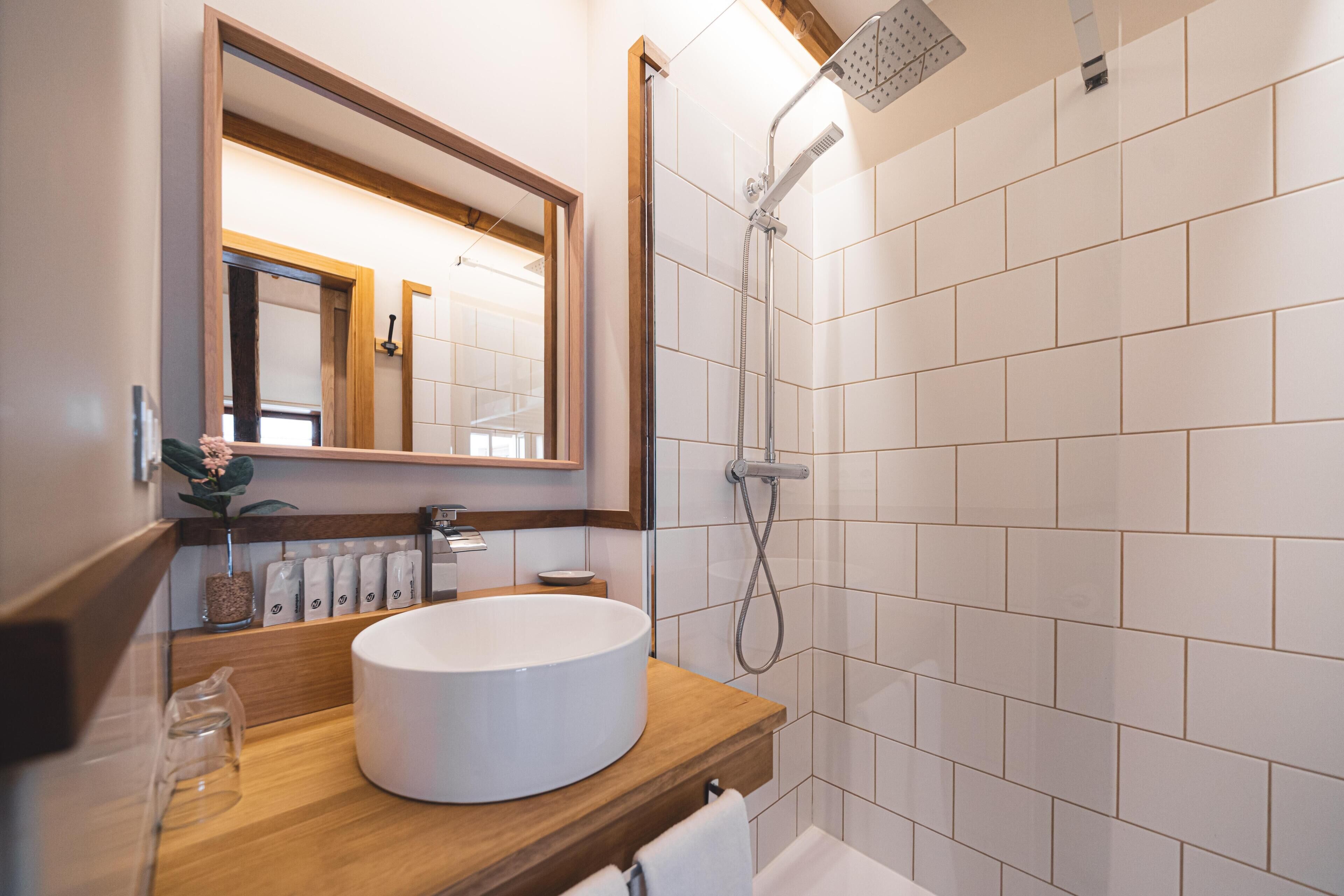 A modern bathroom with a wooden vanity, a round sink, a large mirror, and a shower with a handheld showerhead.