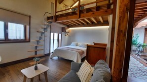 A cozy room with a bed, a small table with a vase, a wooden staircase, and a balcony with a railing. - Room 6 - El Olivar del Cristo (Urda)