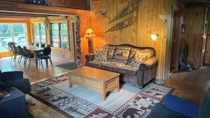 Un interior de cabaña acogedor con una zona de comedor de madera, un sofá con cojines estampados y una alfombra con motivos de animales.