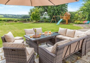 Relax in a serene garden setting with a comfortable sofa and table under a shaded umbrella.